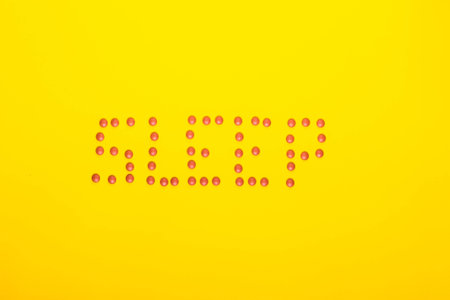 Sleep concept showing sleep spelt in pills on a yellow background