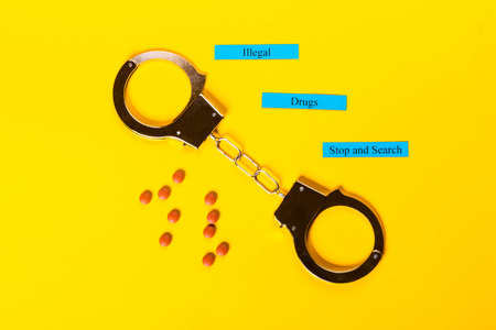 Crime concept showing handcuffs on a yellow background with pills and Illegal Drugs Stop and Searchの写真素材