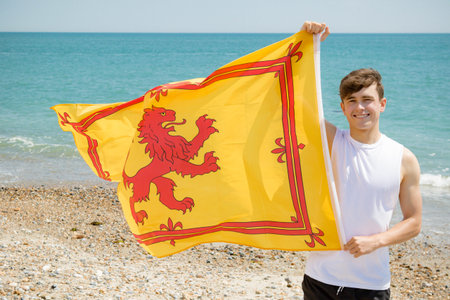 Young adult caucasian male holding on a beach holding the Lion Rampant of Scotland
