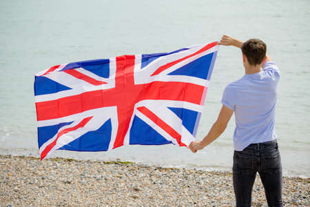 Young adult caucasian male holding on a beach holding the flag of Great Britainの写真素材