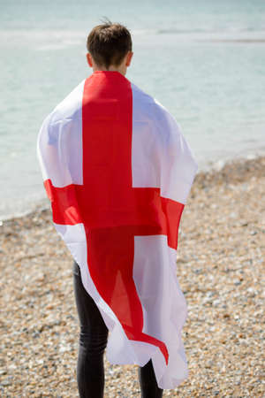 Young adult caucasian male holding on a beach holding the flag of Englandの写真素材