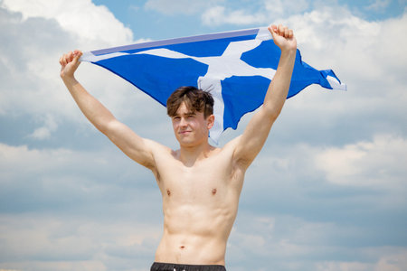 Young adult caucasian male holding on a beach holding the flag of Scotland
