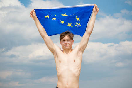 Young adult caucasian male holding on a beach holding the flag of The European Unionの写真素材