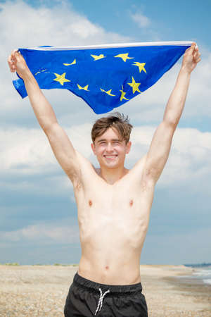 Young adult caucasian male holding on a beach holding the flag of The European Unionの写真素材