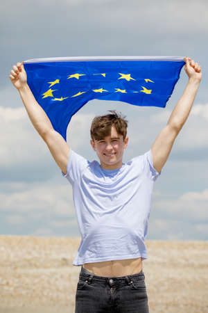 Young adult caucasian male holding on a beach holding the flag of the European Unionの写真素材