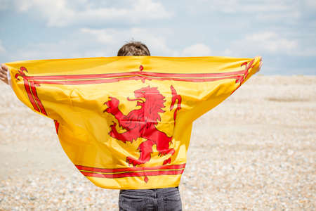 Young adult caucasian male holding on a beach holding the Lion Rampant of Scotlandの写真素材