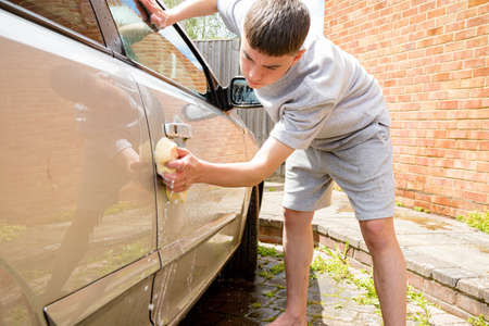 Teenage boy washing a car on a warm summer's dayの写真素材