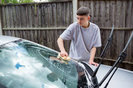 Teenage boy washing a car windscreen on a warm summer's dayの写真素材