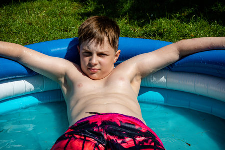 Shirtless preteen caucasian boy laying in a paddling pool