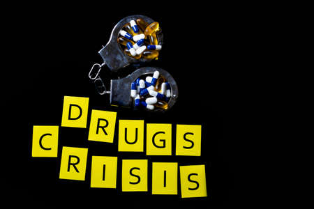 Illegal drug crisis concept showing tablets, handcuffs and the message Drugs and Crisisの写真素材