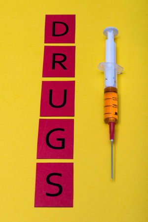 Illegal drug crisis concept showing a full syringe and the message Drugs on a yellow background