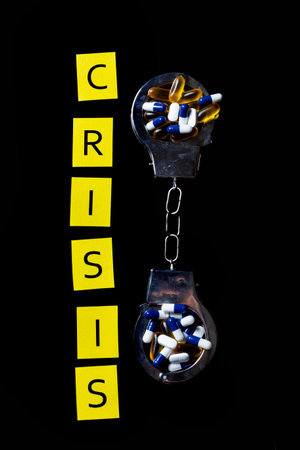Illegal drug crisis concept showing tablets, handcuffs and the message Crisis