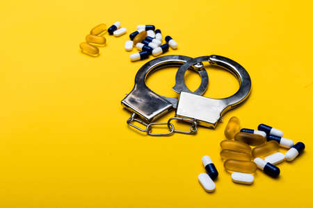 Illegal drug crisis concept showing pills and handcuffs on a yellow backgroundの写真素材