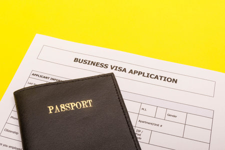 Travel concept showing a passport and an application form for a business visa on a yellow background