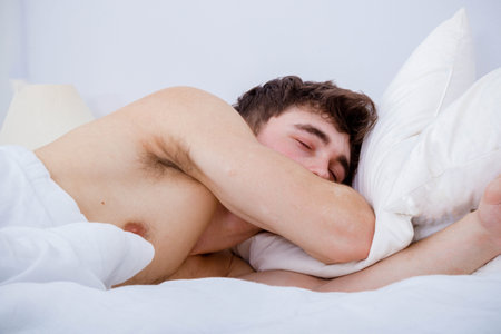 A young adult man sleeping in a bed bare chested