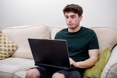 A young adult man on a sofa using a laptop computer