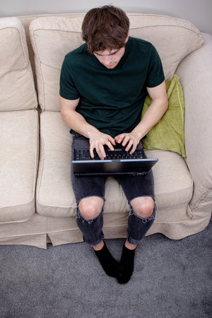 A young adult man on a sofa using a laptop computer