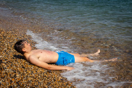 A 18 year old Caucasian shirtless teenage boy laying in the surfの写真素材