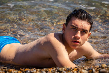 A 18 year old Caucasian shirtless teenage boy laying in the surfの写真素材