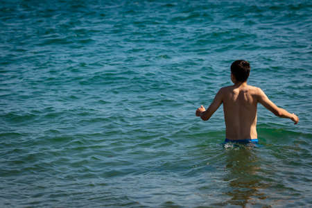 A 18 year old Caucasian shirtless teenage boy in swimwear walking into the seaの写真素材