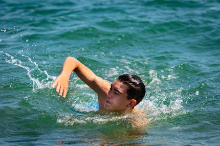 A 18 year old Caucasian shirtless teenage boy in swimwear swimming in the sea