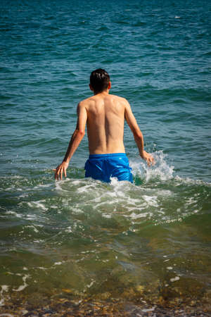 A 18 year old Caucasian shirtless teenage boy in swimwear walking into the seaの写真素材