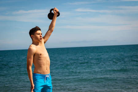 A 18 year old Caucasian shirtless teenage boy in swimwear exercising with a kettlebell weight with copy spaceの写真素材
