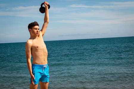 A 18 year old Caucasian shirtless teenage boy in swimwear exercising with a kettlebell weight with copy spaceの写真素材
