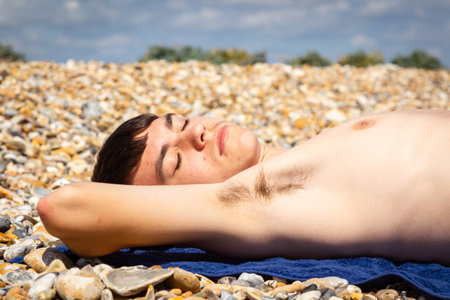 A 18 year old Caucasian shirtless teenage boy sunbathing on a stoney beach