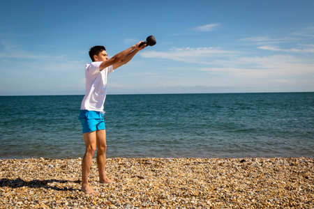 A 18 year old Caucasian teenage boy on a beach exercising with a kettlebell weightの写真素材