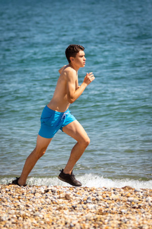 A 18 year old Caucasian shirtless teenage boy running on a beach next to the sea