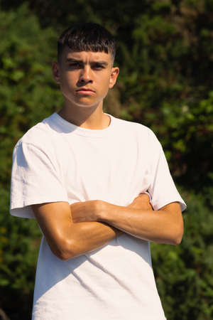 18 year old teen boy in a white t-shirt outdoors with folded armsの写真素材