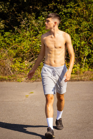 An eighteen year old teenage boy walking outside on a warm summer's day while shirtlessの写真素材