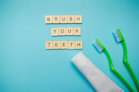 Oral and dental health concept showing two toothbrushes and toothpaste with a sign reading brush your teeth on a blue coloured backgroundの写真素材