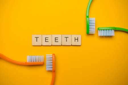 Oral and dental health concept showing four toothbrushes and a sign reading Teeth on a yellow coloured backgroundの写真素材