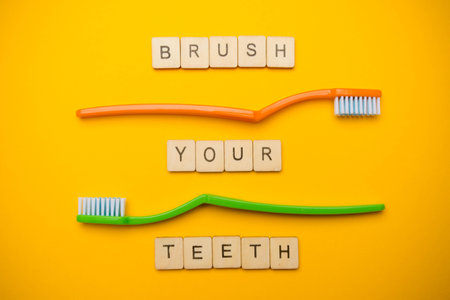 Oral and dental health concept showing two toothbrushes and a sign reading Brush Your Teeth on a yellow coloured backgroundの写真素材