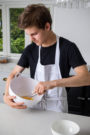A teenage boy in a domestic kitchen whisking eggs