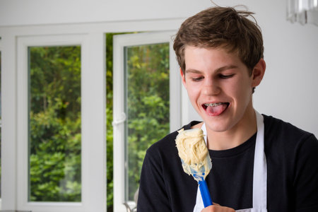 A teenage boy in a domestic kitchen tasting cake mix