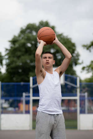 A Nineteen Year Old Teenage Boy Shooting A Hoop in A Basketball Court in A Public Parkの写真素材