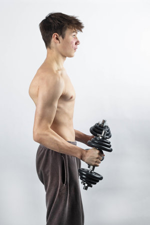 A 17 year old shirtless muscular teenage boy exercising with dumbbellsの写真素材