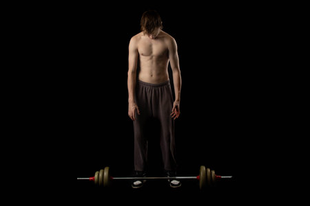 A 17 year old shirtless muscular teenage boy using a barbell