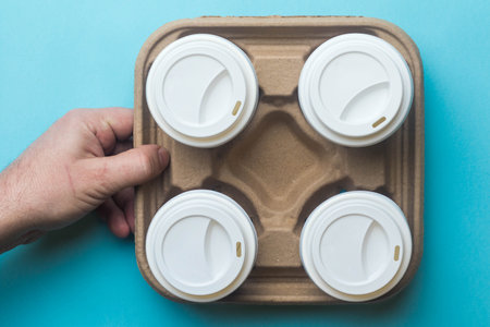 A cardboard tray for carrying paper coffee cups with four cups and lids held by a handの写真素材