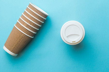A stack of paper coffee cups and a plastic lid on a blue backgroundの写真素材