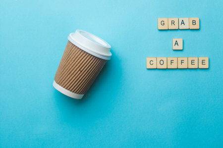 A paper coffee cup and lid on a blue background with a sign reading grab a coffeeの写真素材
