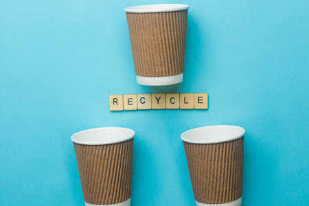 3 empty coffee cups and a sifgn reading recycle on a blue backgroundの写真素材