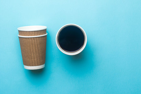 An open cup of black coffee next to a stack of paper coffee cupsの写真素材