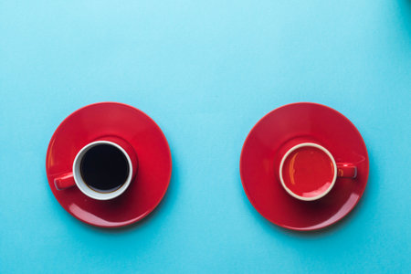 An Espresso cup of black coffee on a saucer next to an empy cup on a blue back groundの写真素材