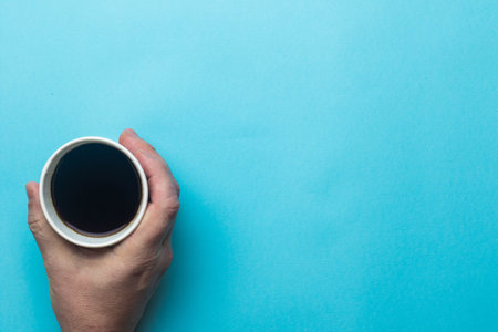 A hand holding an open cup of black coffee
