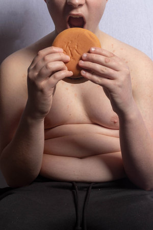 An overweight caucasian teenage boy eating a  burgerの写真素材