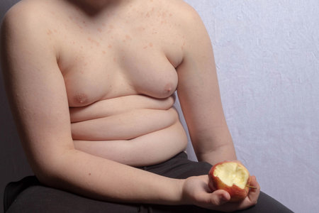An overweight caucasian teenage boy holding an apple with a bite taken outの写真素材